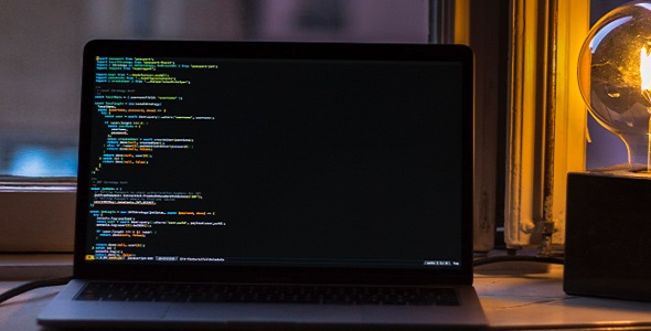 A computer on a desk which shows code on the screen.