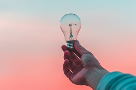 A hand holding a lightbulb to the sky